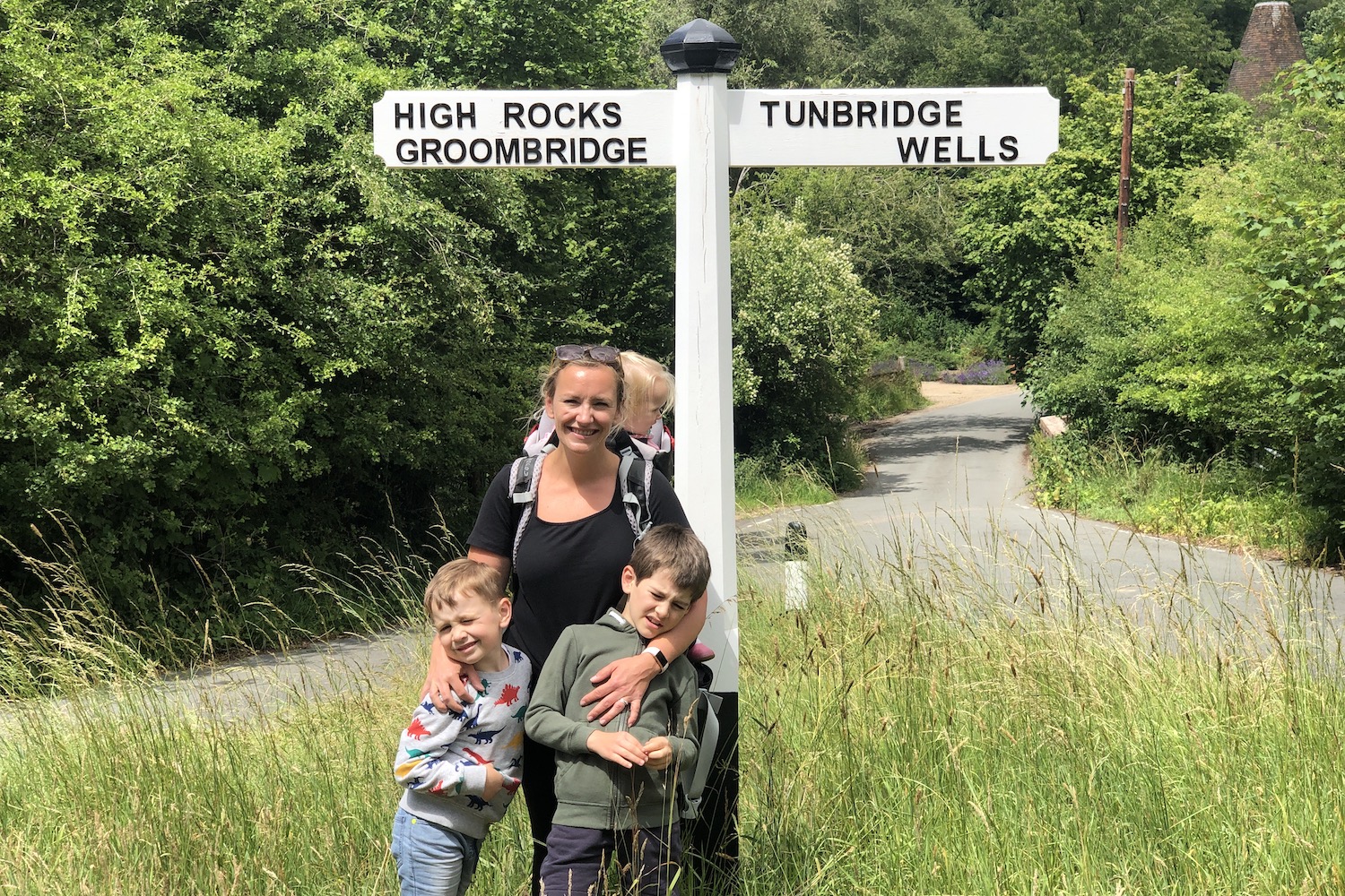 A woman with her three children standing in front of a sign post pointing towards Tunbridge Wells on the right and High Rocks Groombridge on the left