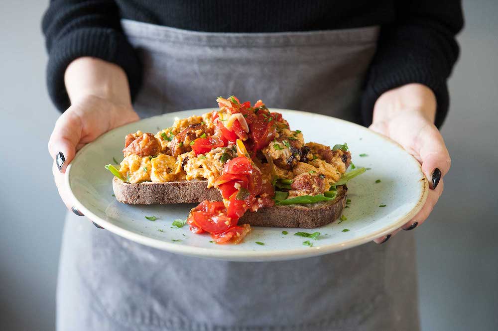 st-kilda-tunbridge-wells a server holding a plate of food with scrambled eggs and tomatoes on two pieces on sourdough