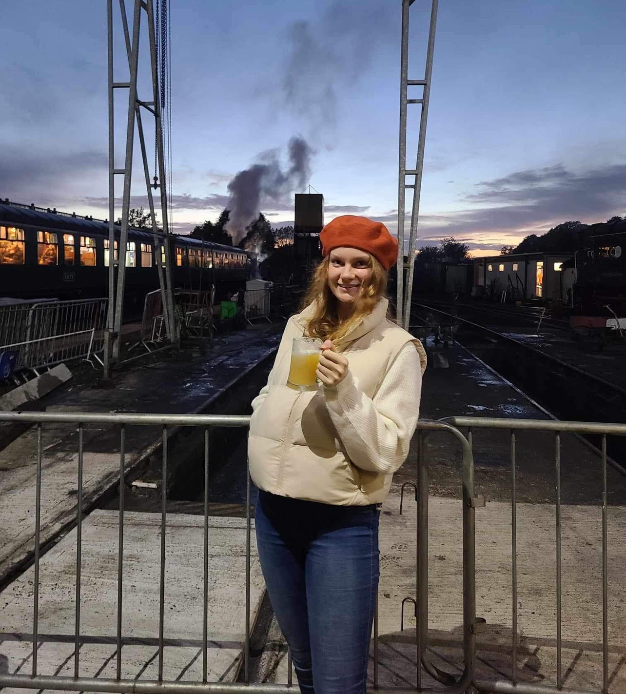 A lady standing with a beer in front of a steam train at the Spa Valley Beer Festival